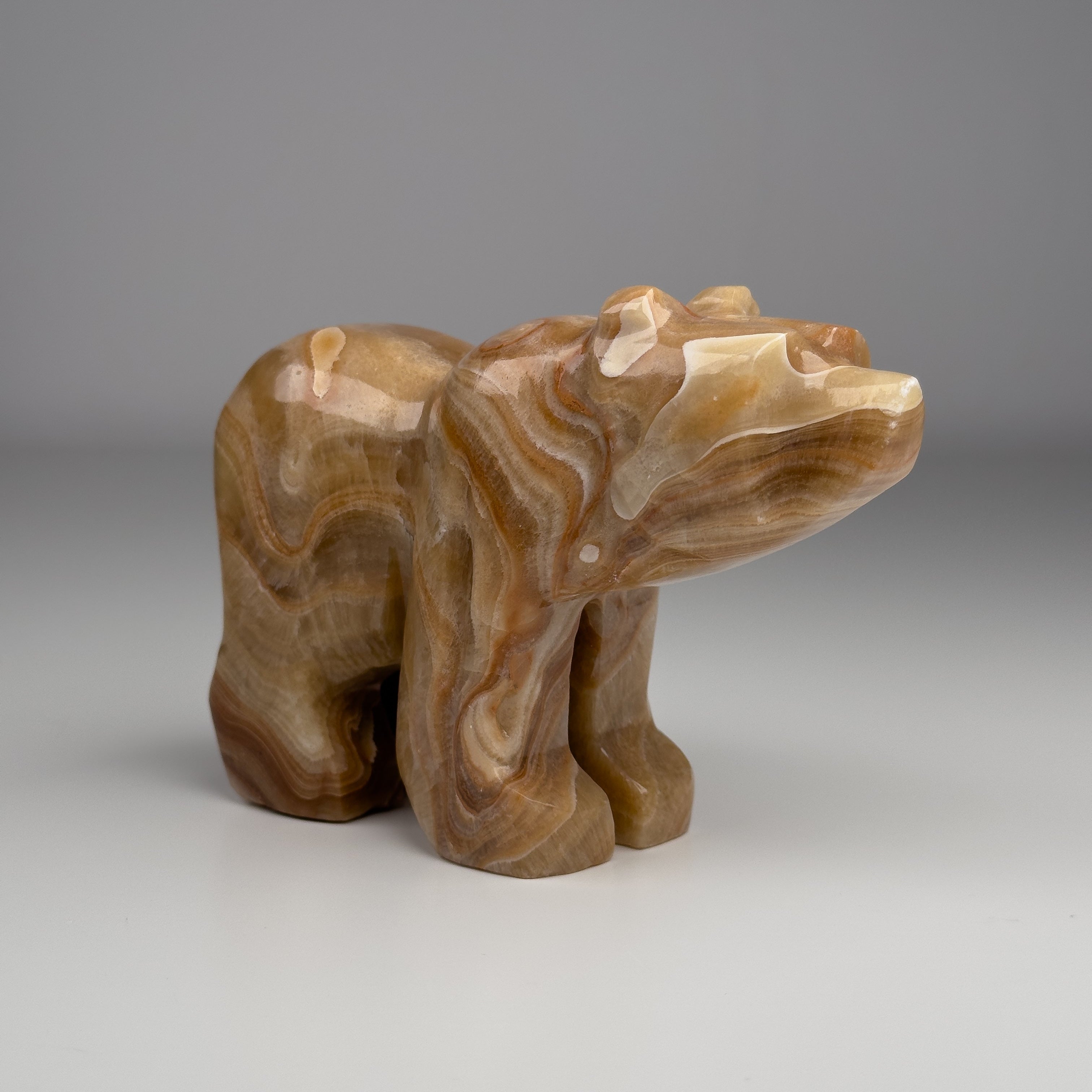 A carved stone sculpture of a bear, with a smooth honey-colored onyx stone surface, displayed against a neutral background.